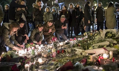 People pray, place flowers and light candles in tribute to the victims of the attacks near the Bataclan concert venue in Paris, France on Saturday. An unprecedented string of attacks in Paris on Friday left at least 120 dead and more than 350 injured.